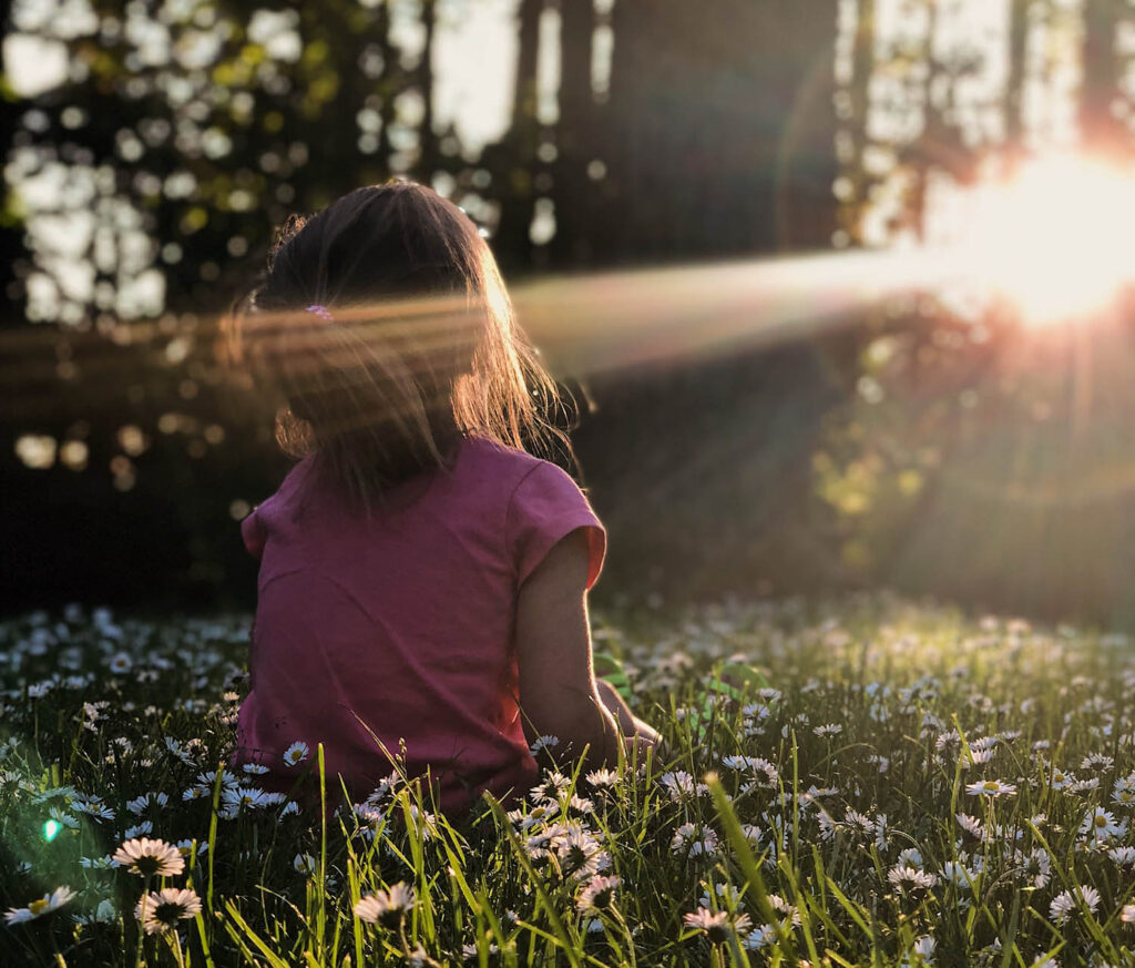 Child connecting with nature, sitting in a ray of sun.